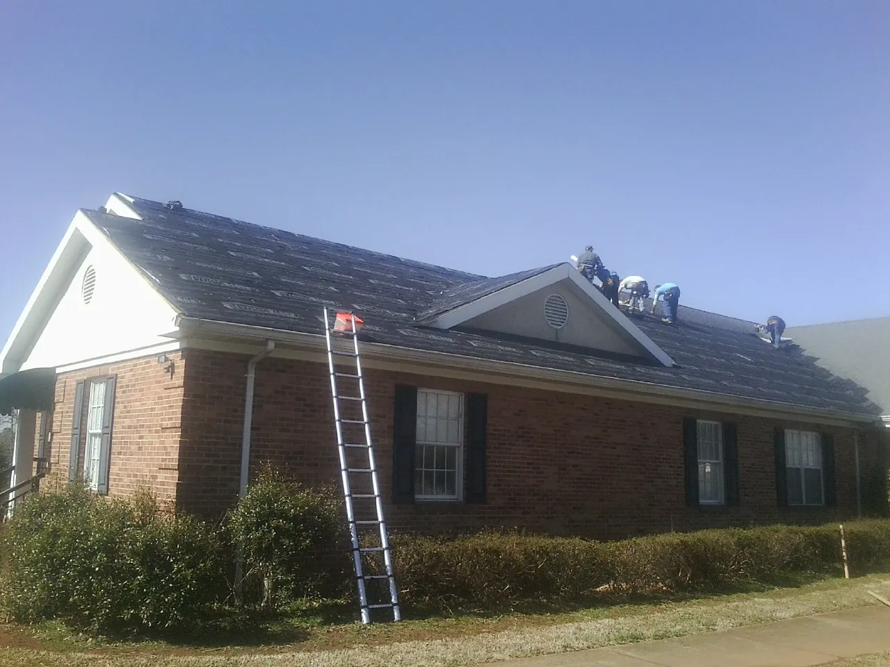 Crew tearing shingles off a brick ranch roof with a ladder set — Metal Roof Repair work by our crew in Suisun City