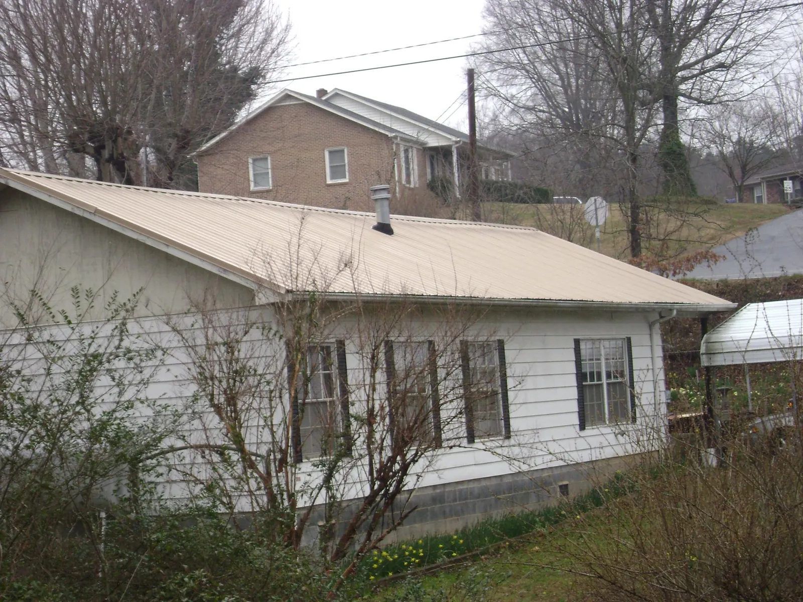 Tan metal roof on a white sided house set into a hillside — Commercial Roofing by Roofing Brothers in Suisun City